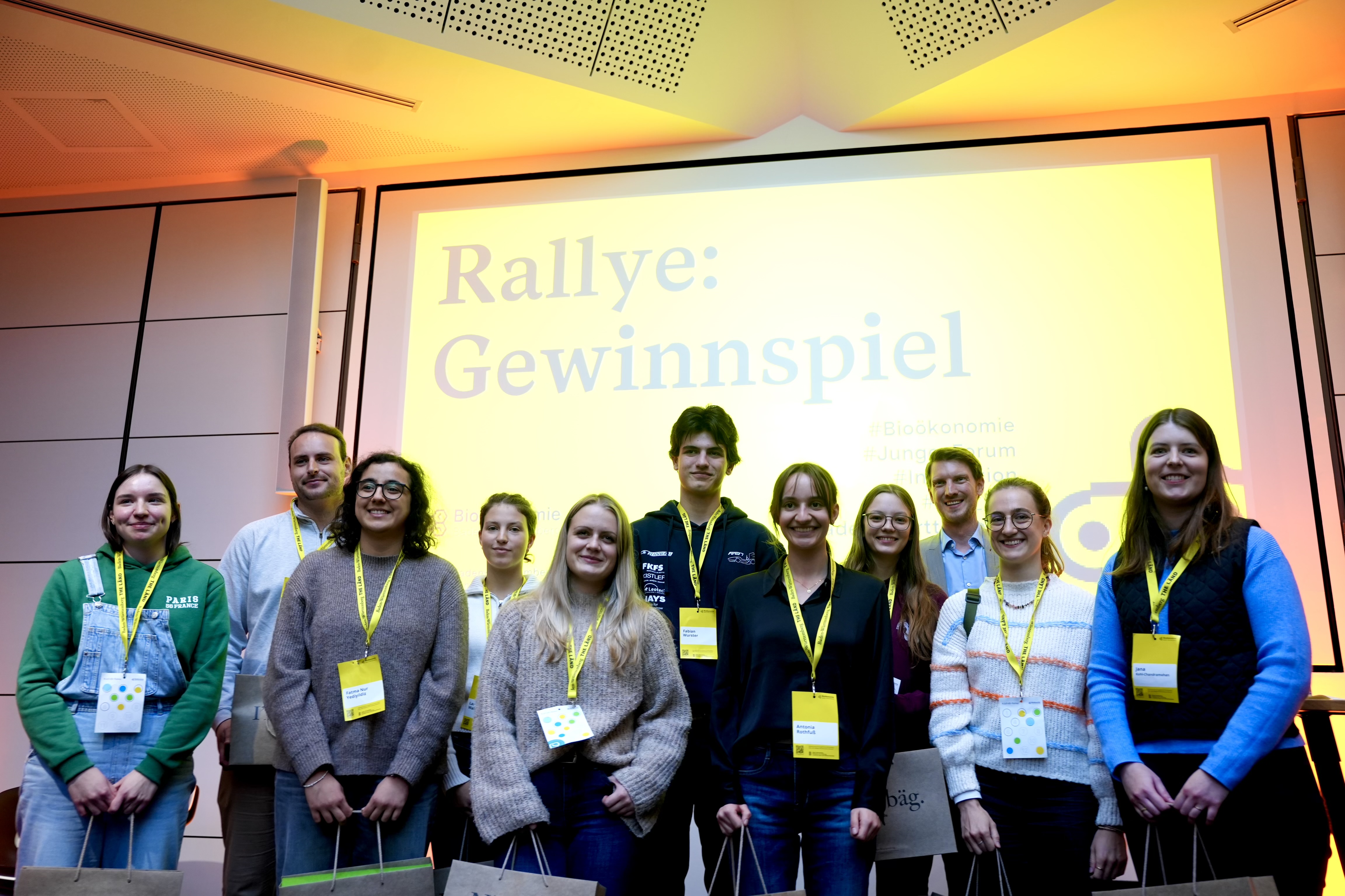 Zehn Gewinnerinnen und Gewinner der Rallye beim Jungen Forum Bioökonomie 2025 auf der Bühne vor einem gelben Hintergrund
